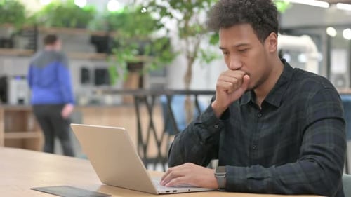 Young Man Coughing While Using Laptop at Work