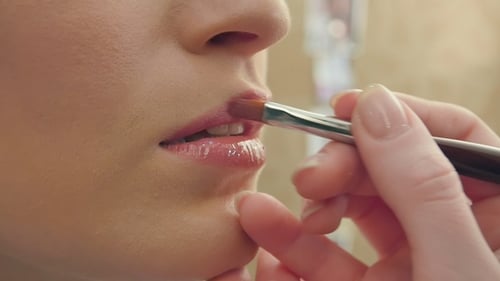 Maskenbildner trägt mit einem Pinsel Lipgloss auf die Modellippen auf
