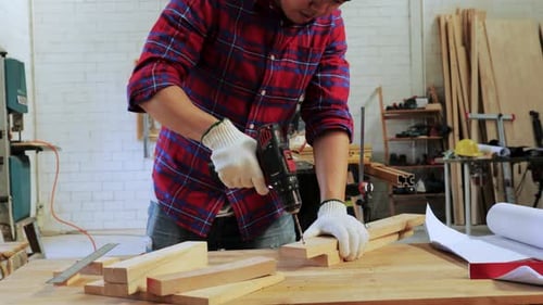 Carpenter drill the wood on the workshop table by a hand drill in wood factory