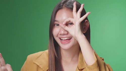 Porträt einer glücklichen asiatischen Frau, die im Greenscreen-Studio vor der Kamera eine Okay-Geste zeigt