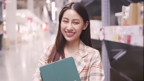Young Woman Holding Tablet Smiling in Warehouse Aisle