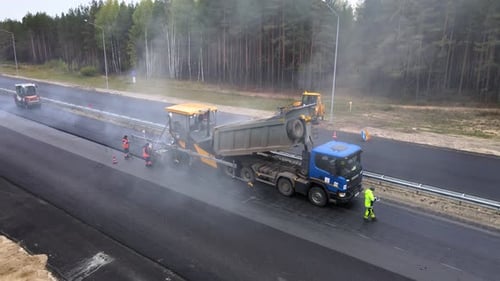 The final stage of road works. Laying the top layer of hot gray tarmac mix