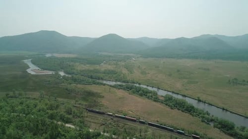 Vista aérea de um trem de carga que passa pela floresta e um rio
