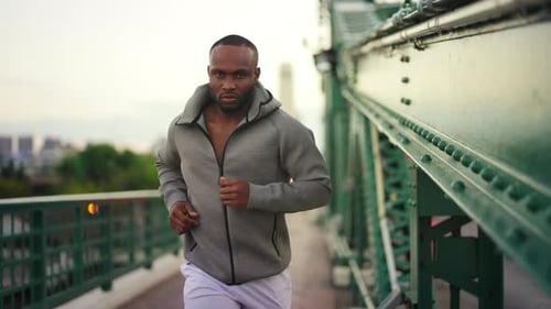 4K African man in sportswear and smart watch jogging on the bridge in the city