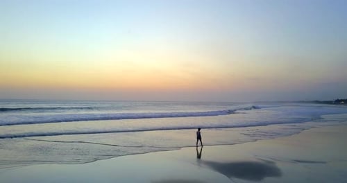 Vista aérea desde un Zumbido de una mujer joven caminando por la playa al atardecer