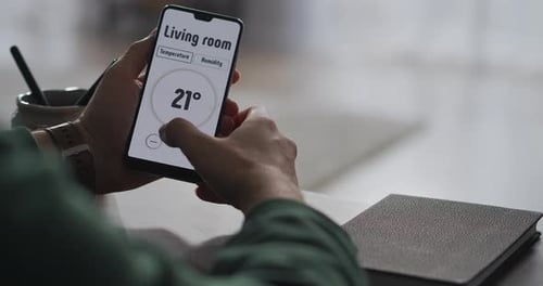 Man is Using Modern App in Smartphone for Controlling Parameters of Smart Home System Closeup View