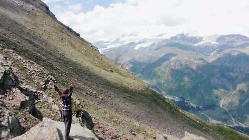 Aerial View of a Female Tourist Standing on the Edge of a Cliff with Her Hands Raised Against the