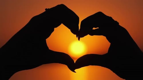 Silueta de manos femeninas sosteniendo un cartel en forma de corazón en una puesta de sol anaranjada