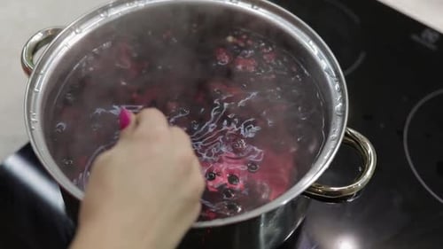 Boiling berries are stirred in stainless steel pot