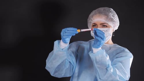 Niña examina un tubo de ensayo con biomaterial. Una mujer joven con ropa protectora. En la cara de un