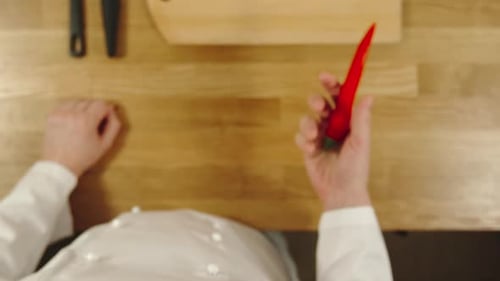 Chef Inspects Red Chili Pepper on Wooden Counter
