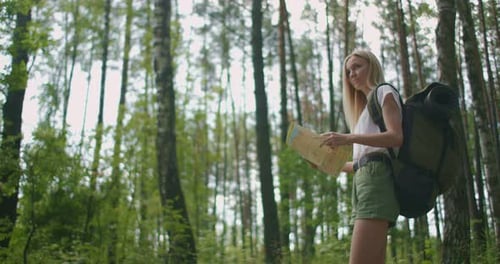 A Young Woman with a Map Walks Through the Forest Traveling with a Backpack in Slow Motion