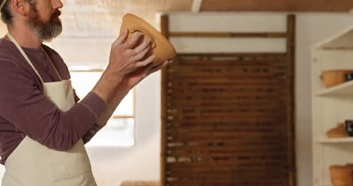 Artisan Inspecting Handmade Pottery in a Studio