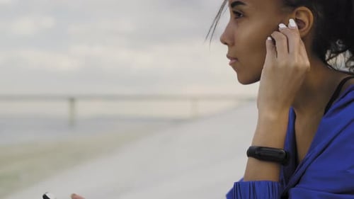 Afro-american Runner Woman with Earphones and Smartwatch Resting After Running in the Park