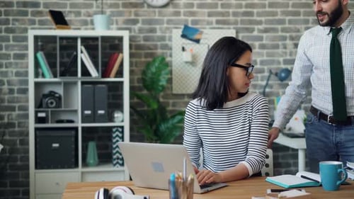 Attraktive Frau arbeitet mit Laptop und diskutiert dann mit einem männlichen Kollegen über die Arbeit
