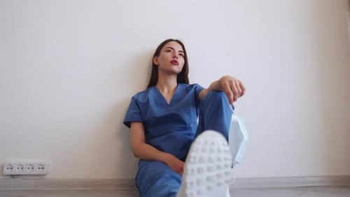 Medical Professional in Scrubs Sitting Indoors Holding Mask