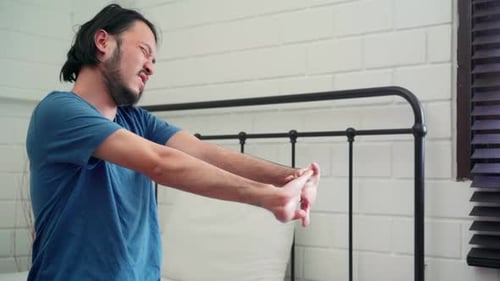 Man Stretches and Rubs Sore Neck on Bed