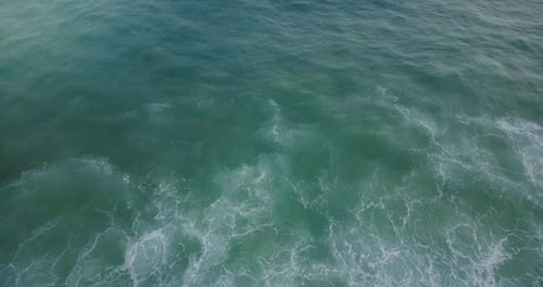 Drone Flying Backwards Behind an Ocean Wave Over Amazing Natural Seafoam Texture of Blue and Mint