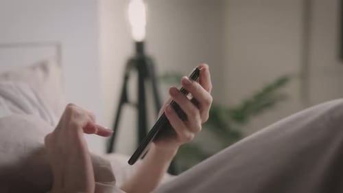 Unrecognizable Woman Uses Smartphone While Lying in Bedroom
