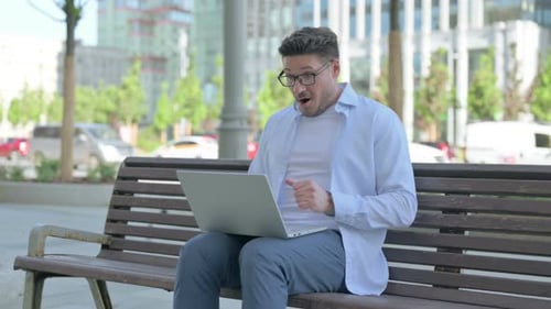Man Celebrates Laptop Success on City Bench
