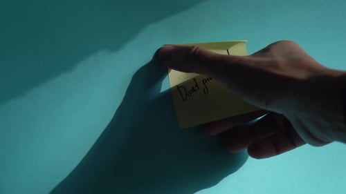 Hand places motivational sticky note on blue background