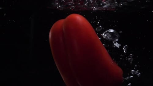 Rote Paprika fällt ins Wasser. Zeitlupe. Schwarzer Hintergrund. Video zum Thema Essen