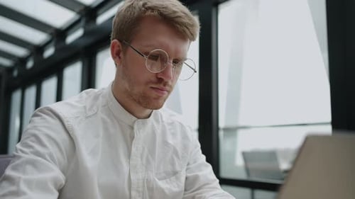 Handsome Young Busy Male Office Worker Sitting at Table and Working on Laptop Computer