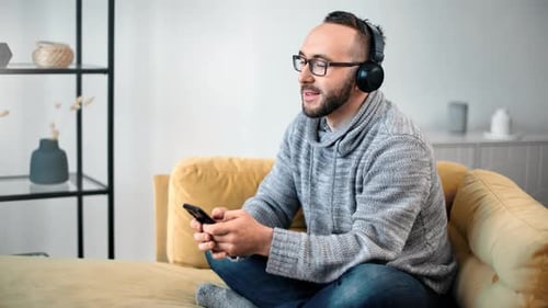 Man Relaxing on Couch Listening Music and Using Phone