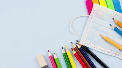 Schulmaterial mit Notizblock liegt auf einem pastellblauen Hintergrund mit einer medizinischen Maske