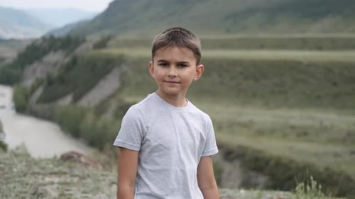 Little Boy Tourist Looking at the Camera on a Background of Mountains and a River
