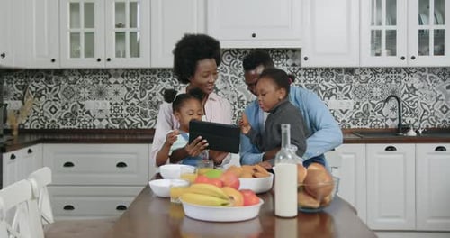 Familia afroamericana sentada alrededor de la mesa y usando una tableta