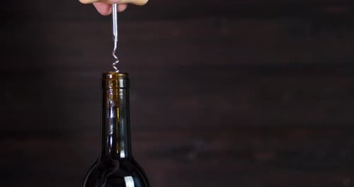 El sacacorchos para hombre abre una botella de vino. Sobre un fondo de madera.