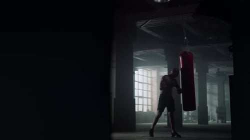 Muscular Man Punches Heavy Bag in Urban Gym