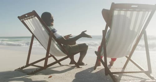Smiling senior african american couple lying on sunbeds on sunny beach