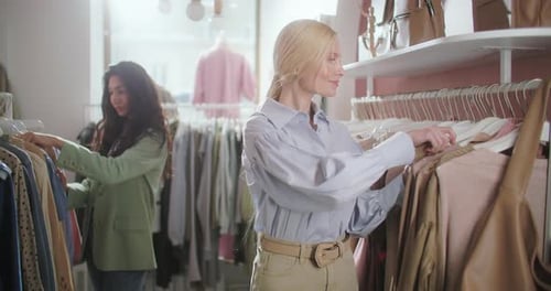 Pretty Young Blonde Woman Choosing Clothes in a Clothing Store