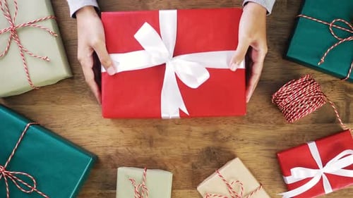 Person Places Holiday Gift on Table with Presents
