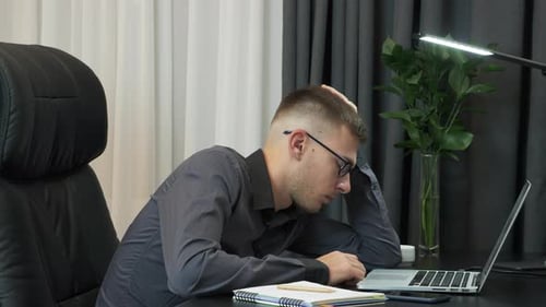 Man Tired at Desk Looking at Laptop