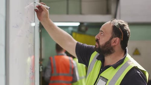 Caucasian male factory worker at a factory writing on white board