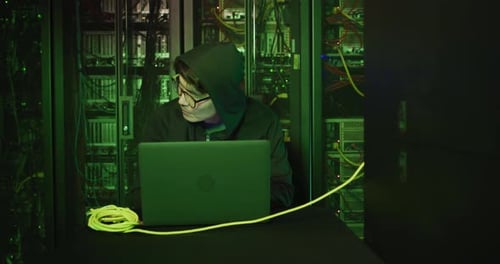 Asiatischer männlicher Hacker im Hoodie benutzt Laptop von Computerservern