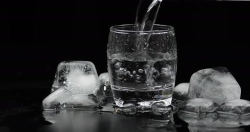 Water Being Poured into Glass Surrounded by Ice
