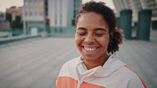 Smiling Woman in City Wearing Athletic Jacket and Headphones