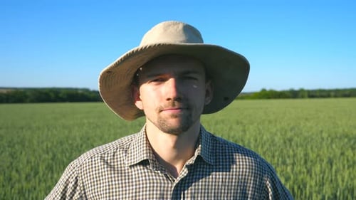 Portrait of Confident Farmer in Hat Looking Into the Camera Against the Background of Green Wheat