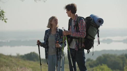 20s Couple Hiking on the River Side with Tourist Backpack and Trekking Poles Early in the Morning