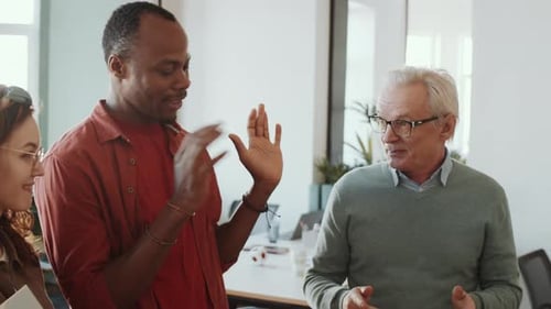 Elderly Manager Speaking with Young Employees in Office