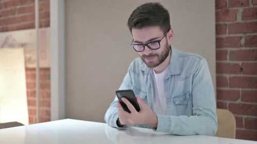 Attractive Young Male Designer Using Smart Phone in Office