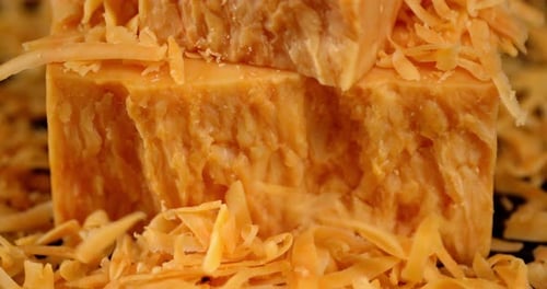 Kleine Stücke geriebener Cheddar-Käse fallen auf den Tisch