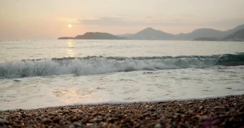 Nahaufnahme von Meereswellen, die den Kieselstrand beim Sonnenuntergang in Montenegro waschen