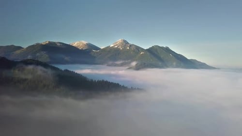 Fliegen Sie über nebligen Wolken in sonnigen Bergen