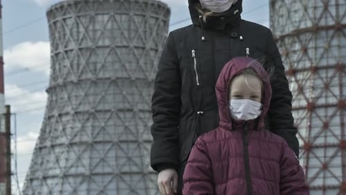 Mama mit einem kleinen Mädchen in Masken auf dem Hintergrund eines Wärmekraftwerks