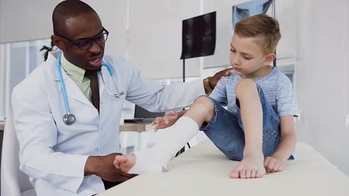 Caring Doctor Bandaging Child's Leg in Clinic